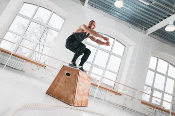 Bearded athlete male jumping over wooden box in sport gym. Fit man doing jump exercises for strong...