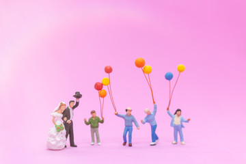 Miniature people, Couple and family with colorful balloons celebrating on pink background