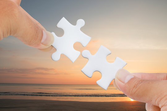 hands trying to connect jigsaw puzzle piece with sea and beach background.