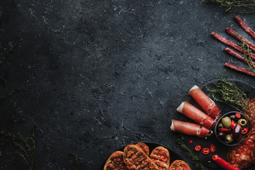 Mediterranean appetizers. Jamon, chorizo, fuet and crispbread on dark background with copy space.
