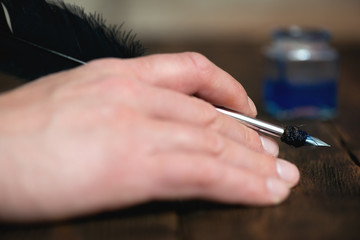 A writer is holding a quill pen in hand on a wooden desk background.
