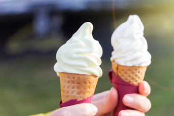 Woman's hands holding melting ice cream waffle cone in hands on summer light nature background