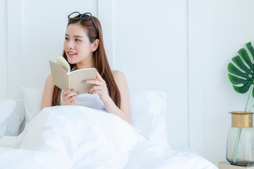 Fototapeta na wymiar beautiful attractive asian woman enjoy reading book on bed portrait of asian long hair woman enjoy weekend activity white bedroom