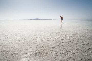 Young woman standing in white salt lake looking towards the horizon