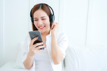 beautiful attractive asian woman listen song from headphone hand hold smartphone white bedroom background portrait of asian long hair white shirt woman