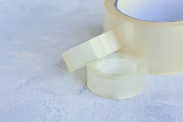 Set of glue packing tape with selective focus on grey cement background. Repair plastic tapes on neutral surface. Bobbin with transparent sticky sellotape. Fix or packaging tapes