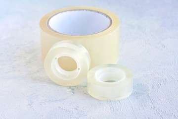 Set of glue packing tape with selective focus on grey cement background. Repair plastic tapes on neutral surface. Bobbin with transparent sticky sellotape. Fix or packaging tapes