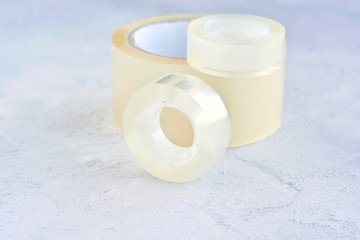 Set of glue packing tape with selective focus on grey cement background. Repair plastic tapes on neutral surface. Bobbin with transparent sticky sellotape. Fix or packaging tapes
