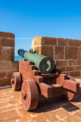 Fototapeta na wymiar View on Fort with old Historical portugese Metal Cannons In a Fortress. Walls with cannons and tower of the old fort in the port and coast of the historic city of Mogador