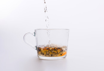 Water pouring into glass cup with tea and slices of orange isolated on white