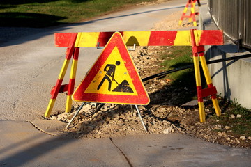 Red and yellow work ahead road sign placed next to paved road and concrete metal fence on warm sunny spring day