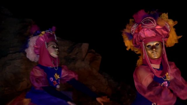 two young girls dancers in bright costumes with flowers and gold masks dance waving their hands. they dance at night before the tongues of fire.