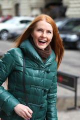 Portrait of pretty sexy young red hair woman in green down jacket posing on spring street