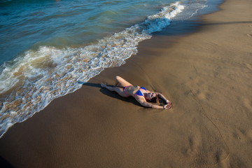 A young woman in a seductive bikini lying on the beach. Girl lying on the sand by the ocean