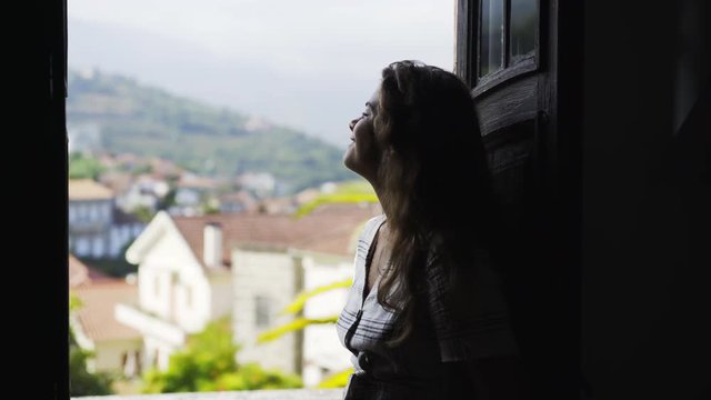 Side view of young cheerful woman on balcony of traditional country house with dark room in valley of Douro river in winemaking region in Portugal
