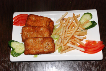 Fried fish cutlets with French fries and vegetables on the white plate