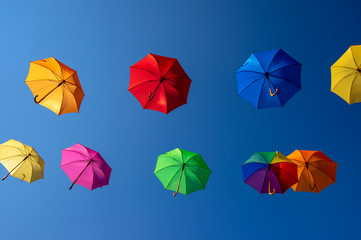 Group of flying umbrellas isolated on blue background, ready for the rain, wallpaper background, bright various colors