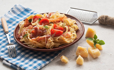 Classic pasta Carbonara, with bacon, egg, Parmesan cheese and Basil on a light background. Pieces of Parmesan, Basil and cheese grater are next to the table.