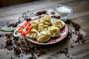 a dish of meat dumplings. Traditional russian pelmeni, ravioli, dumplings with meat on black concrete background. Parsley, quail eggs, pepper, rosemary, bay leaf and spices. 