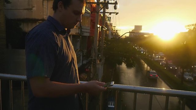 Young handsome businessman goes on a bridge uses a phone during rain and amazing sunset. slow motion. 1920x1080