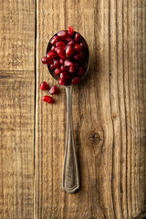 Pomegranate seeds in spoon on rustic wooden background. Detox, diet, fruits ingredient, cooking healthy food or dessert.