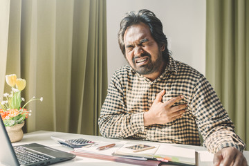 office syndrome concept; businessman sitting at office desk,  suffering from backache after working,man touching lower back with pained expression.