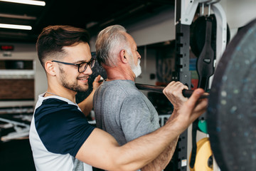 Senior man exercising in gym with his personal trainer.