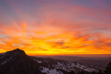 Colorful clouds at sunset in rural landscape with hills and forest. Sky glowing in red, orange and yellow. Bavaria, Germany