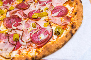 Fresh pizza on thin dough with salami, ham, bacon, pepperoni and onion