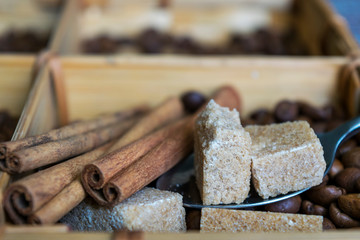 Lots of coffee beans, sugar cubes and cinnamon sticks by wooden box.