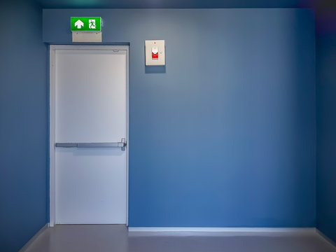 Fire exit door and emergency red light alarm box on blue wall in modern style building.