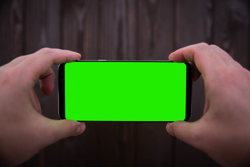 hand holding black cellphone with green screen isolated on wooden background