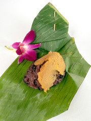 Thai fevorite dessert,Black sticky rice topping with egg custard wrapped in banana leaf packag,Isolated image.