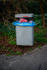 A metal trash can on a path full of plastic garbage