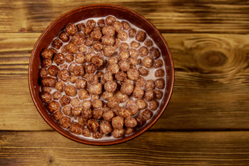 Cereal chocolate balls with milk in a bowl on wooden table. Top view