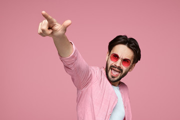 Portrait of a happy cheerful hipster male in pink shirt pointing finger at camera, screaming and...
