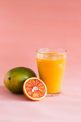 Mango and orange smoothie in glass on pink background.