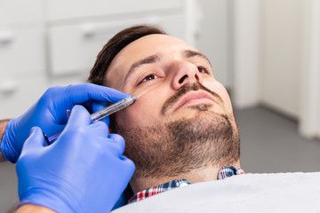 Handsome young man is getting a rejuvenating facial injections. He is sitting calmly at clinic. The expert beautician is filling male wrinkles by hyaluronic acid.