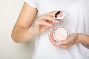 Female hands holding highlighting powder with a puff over a white background