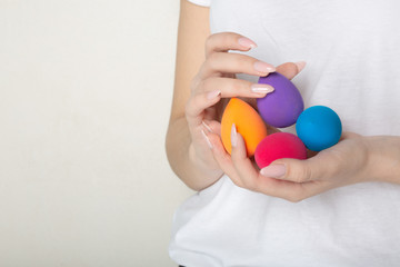 Naklejka premium Woman with nice manicure holding colorful beauty blenders. Empty space
