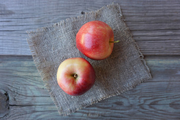 2 fresh red apples on a burlap over the old wooden table. Fruit harvest. 