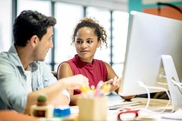 Two young colleagues in smart casual wear discussing something while spending time in the office,African girls learn to work from handsome man by computer