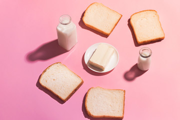 Butter on ceramic plate surrounded by bread and milk on pink background