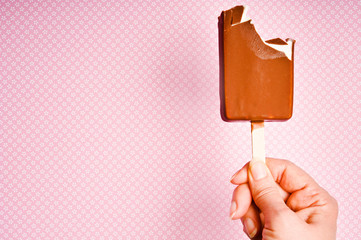 bitten off ice lolly with vanilla icecream and chocolate kept by a female hand over pink background