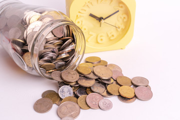 Coins in glass jar and yellow alarm clock isolated on white background. Future financial concept.