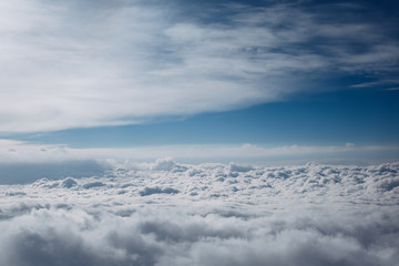 Airplane window view over horizon covered by white clouds beneath sunny blue sky. 