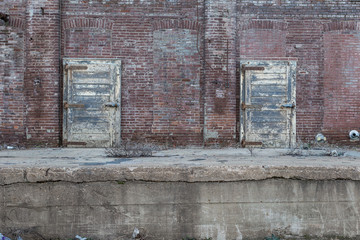 Two large vintage doors on the back of an abandoned crumbling red brick warehouse