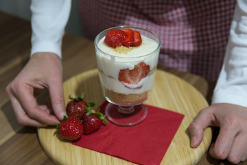layered dessert or Magnolia with strawberries, biscuit cake and cream cheese on a white wood background.