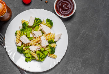 fusilli pasta with chicken breast and broccoli salad in white plate on Dark grey black slate background