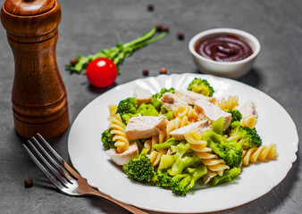 fusilli pasta with chicken breast and broccoli salad in white plate on Dark grey black slate background